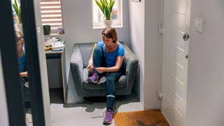 Woman sitting in hallway tying up running shoes