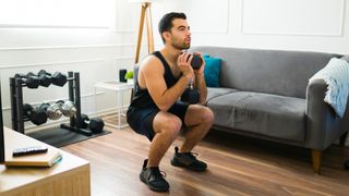 Man performing squat at home, holding dumbbell by his chest