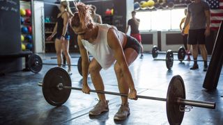 Woman in gym holding barbell resting on floor